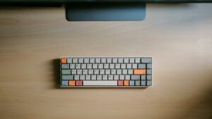 Compact gray keyboard with orange keys on a wooden desk.