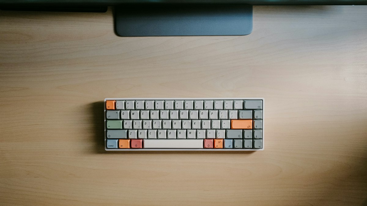 Compact gray keyboard with orange keys on a wooden desk.